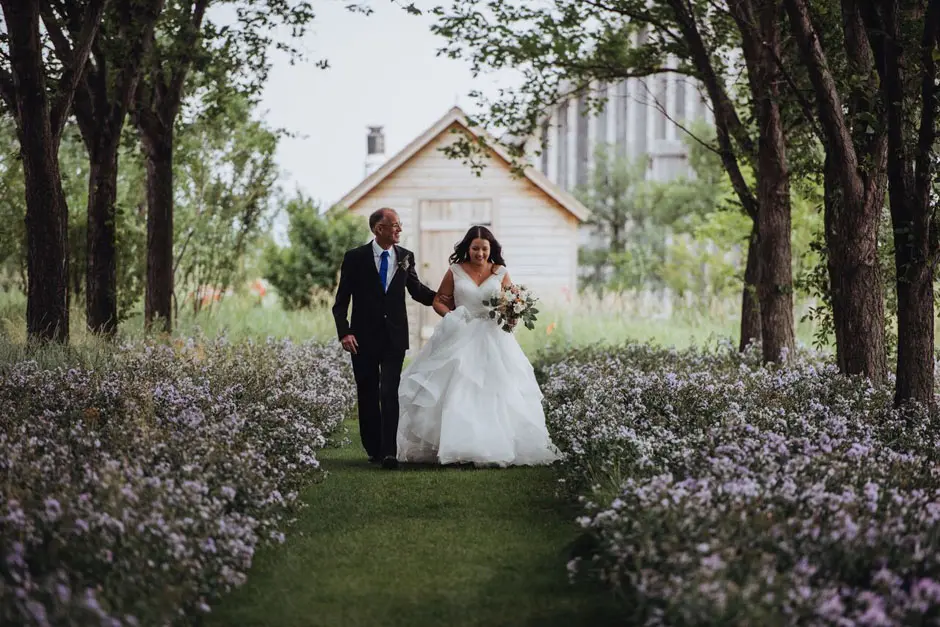 A bride and her father walking down a treed aisle at the Coutts Centre for Western Heritage